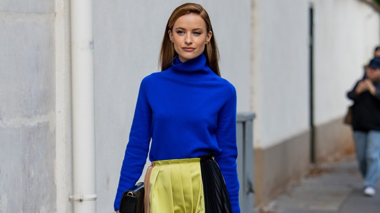 Victoria Magrath wears a cobalt blue turtleneck sweater and yellow pleated skirt during Paris Fashion Week in September 2023