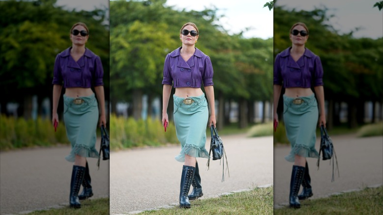 A woman wearing black embellished boots and a blue midi skirt.