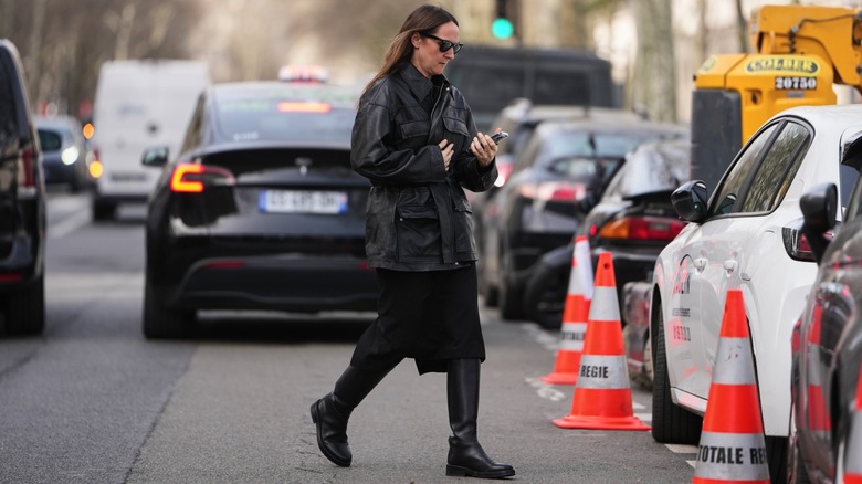 A woman wearing a black leather jacket, midi skirt, and boots.