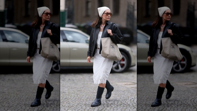 A woman wearing black rain boots and a white midi skirt.