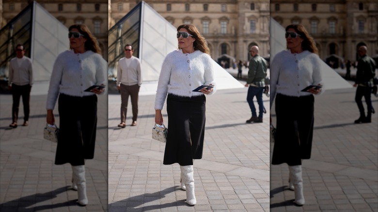 A woman wearing a black A-line skirt and white leather boots.