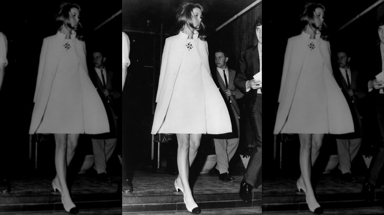 Jean Shrimpton walks wearing a white minidress