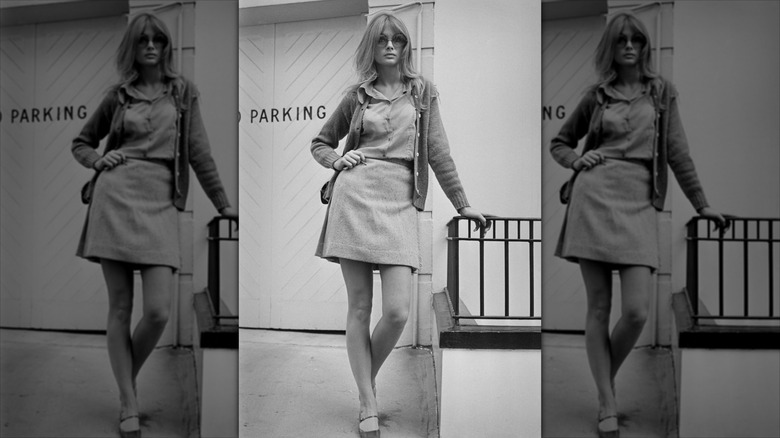 Jean Shrimpton  poses with her hand on her hip wearing a short skirt and big sunglasses