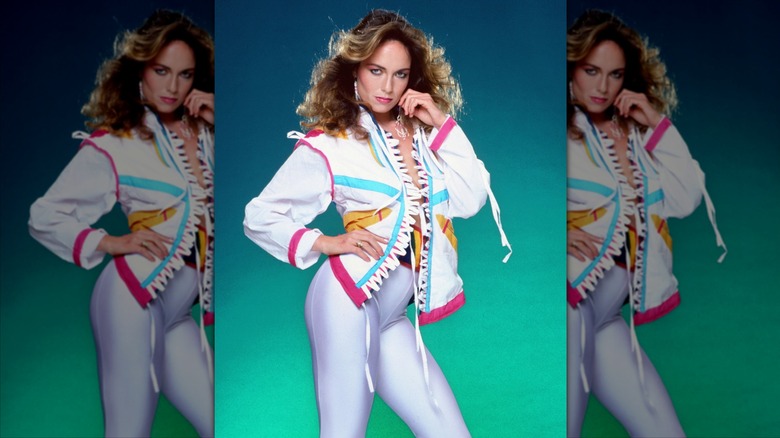 Catherine Bach poses wearing shiny white leggings and a neon bomber jacket