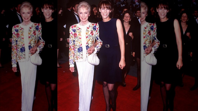 Janet Leigh wearing a white outfit with an ornate floral jacket posing with Jamie Lee Curtis wearing a black, belted dress in February 1995.