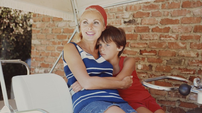 Janet Leigh wearing a blue-and-white striped top and denim shorts with a red headband with daughter Jamie Lee Curtis wearing a red outfit in 1967.