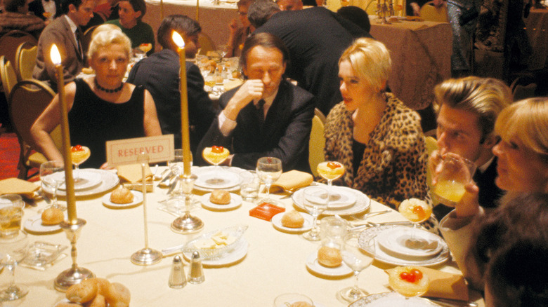 Edie Sedgwick sitting at a table at an event wearing a leopard-print coat.