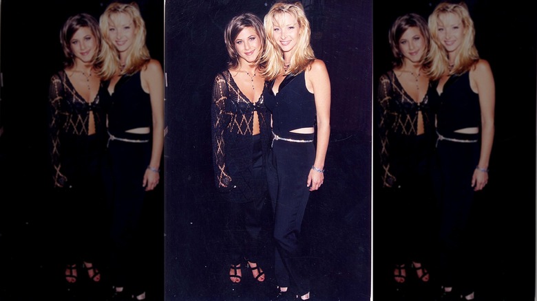 Lisa Kudrow in black pants and a black mini vest posing next to Jennifer Aniston.