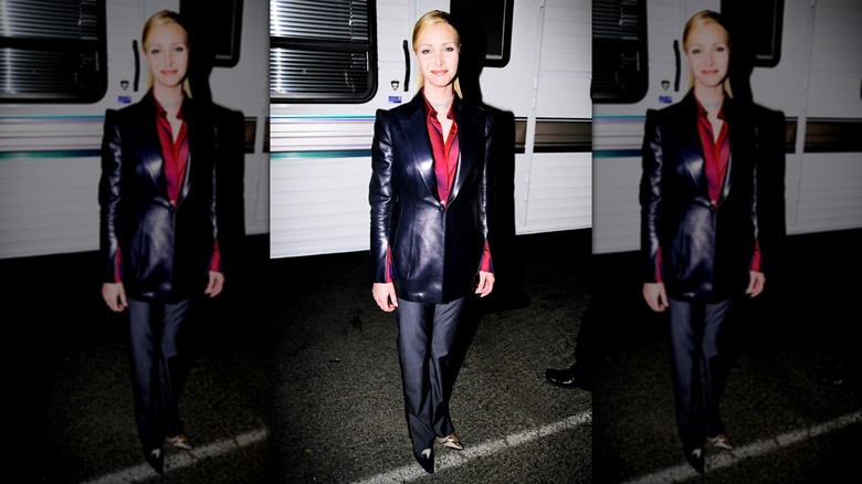 Lisa Kudrow wearing a black leather jacket with a red shirt and gray slacks with slicked-back hair.