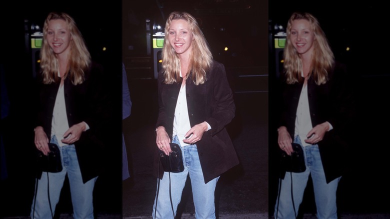 Lisa Kudrow wearing jeans, a white shirt, and a black jacket, with long wavy hair.