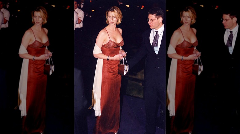Lisa Kudrow posing at a red carpet event in a red dress with a white scarf and short hair.