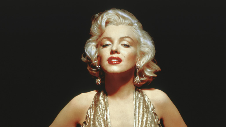 Marilyn Monroe posing in a gold dress with red lipstick in front of a black background