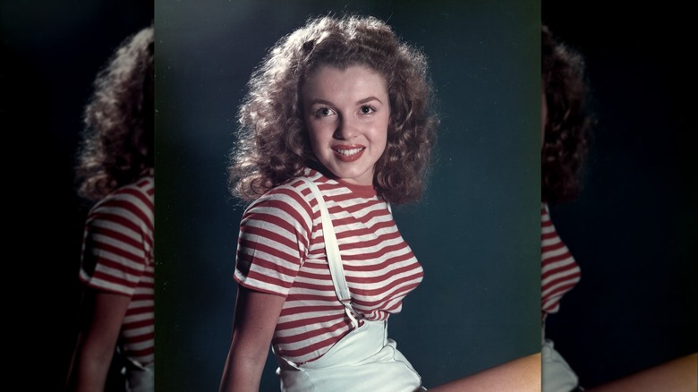 Marilyn Monroe posing in 1947 wearing a red-and-white striped shirt and white suspender shorts.
