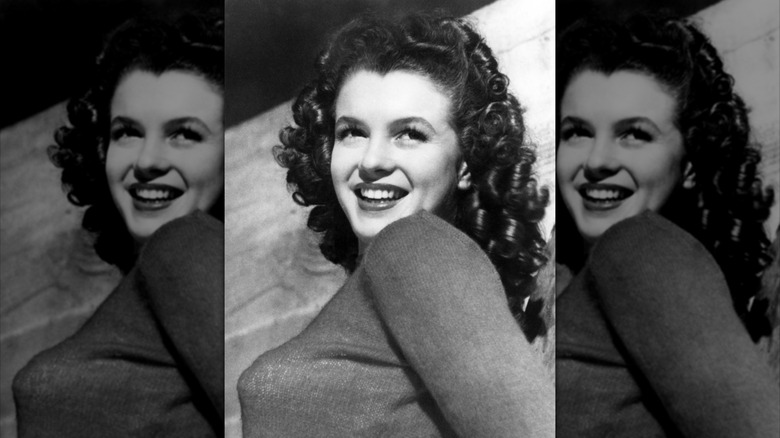 Black-and-white photo of Marilyn Monroe smiling and looking over her shoulder with brown curly hair.