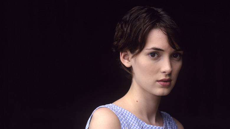 Winona Ryder posing with short hair and a gingham top against a black bakground.