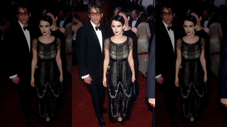 Winona Ryder posing on a red carpet wearing an ornate black dress and slicked-down hair.