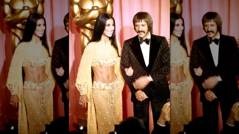 Cher wearing a sparkly gold two-piece posing arm-in-arm with Sonny Bono wearing a brown patterned tux.