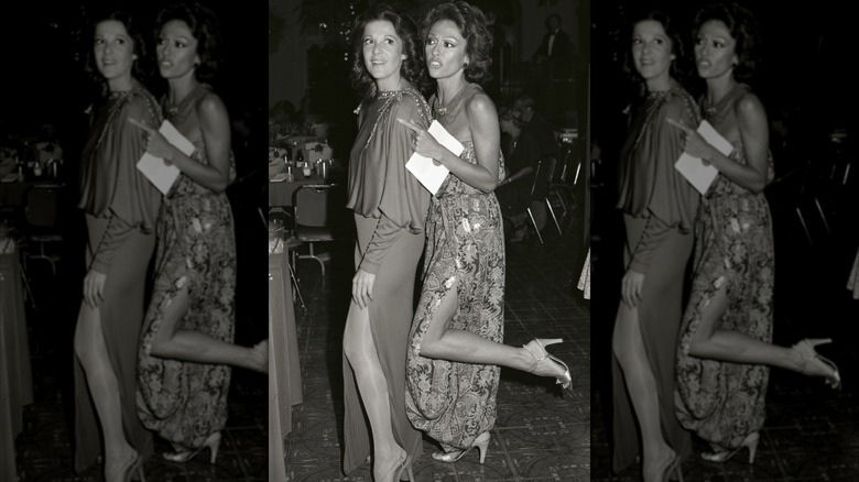Rita Moreno wearing a strapless floral dress with her leg kicked back and Linda Lavin wearing a flowy dress at the 1978 Emmy Awards.