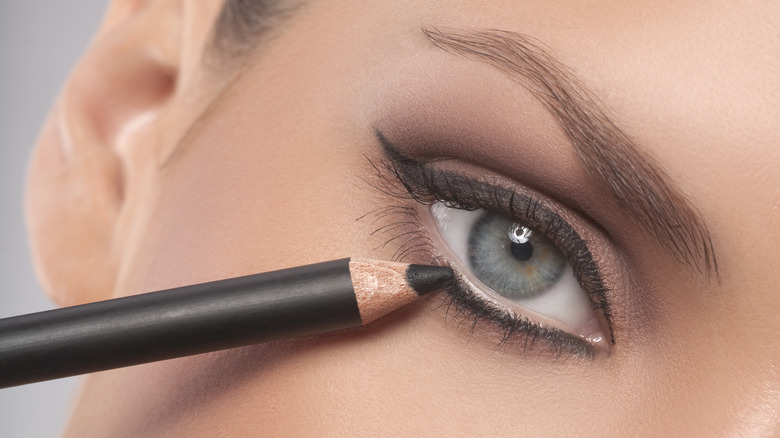 Woman applying pencil eyeliner