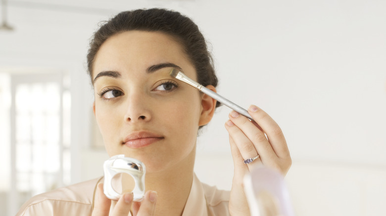 Woman applying makeup in mirror