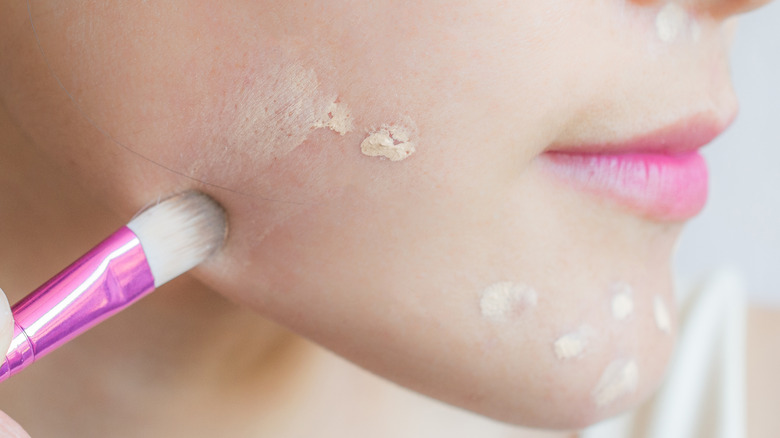 Woman applying concealer on face