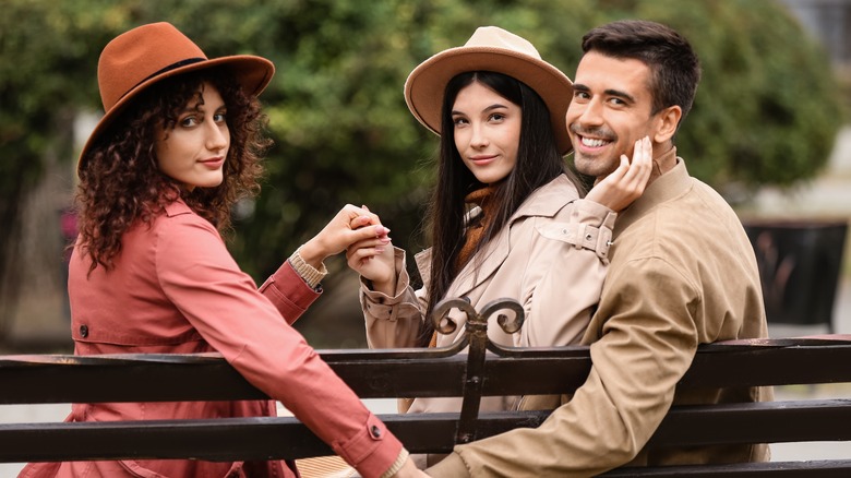 Two women and man smiling and holding hands on bench