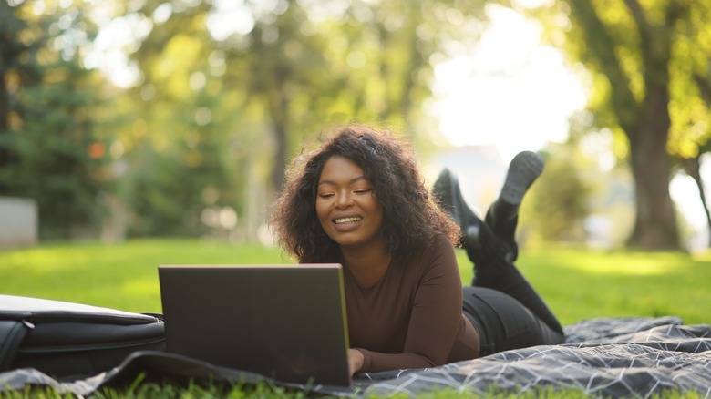 Woman lying in grass typing