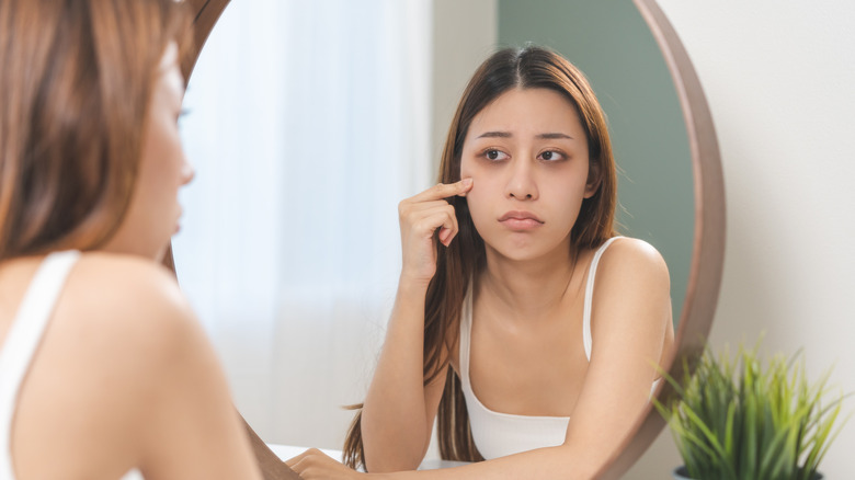 A person examining their puffy eyes and eye bags in the mirror