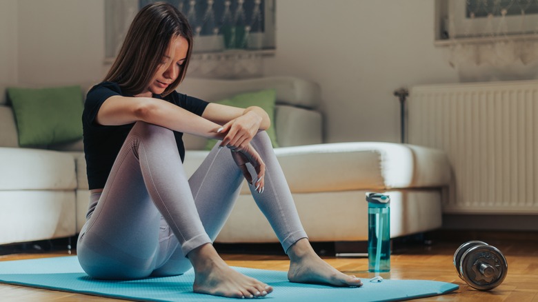 Woman sits on yoga mat and contemplates working out
