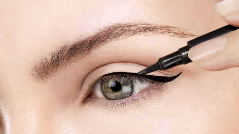 Closeup of a person applying a black eyeliner wing with their eye open