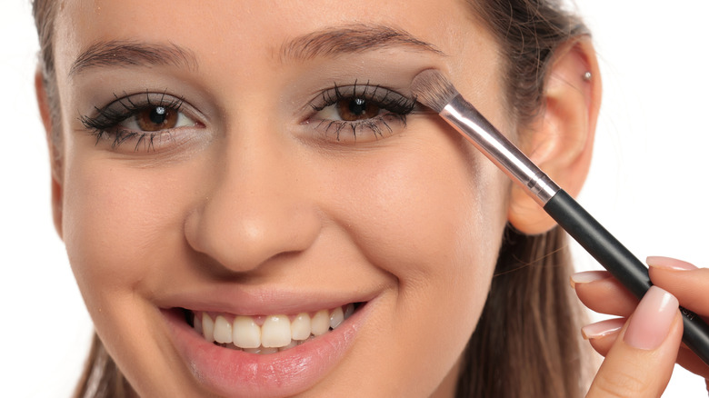 Woman smiling and looking into the camera while applying eyeshadow with a small brush
