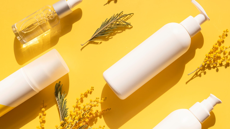 bottles of skincare lay flat on a yellow background surrounded by plants and flowers