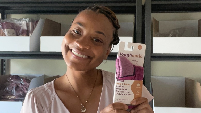 ToughCutie founder Brittany Coleman wears her hair up along with a light pink t-shirt and small hoop earrings while showing off a new color of socks in July 2025.