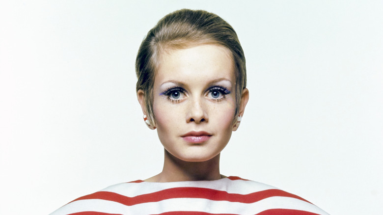 Twiggy poses for a photo shoot wearing blue eyeshadow and a red and white striped top.