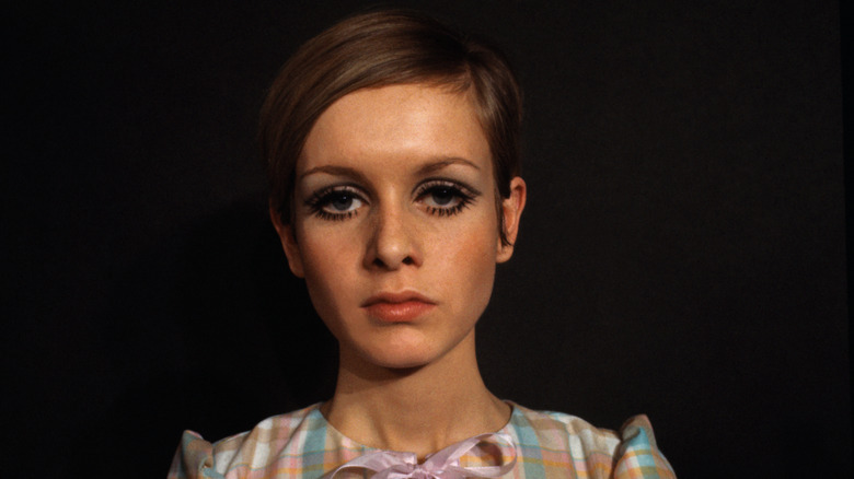 Twiggy poses for a photoshoot wearing bold eye makeup and a gingham shirt