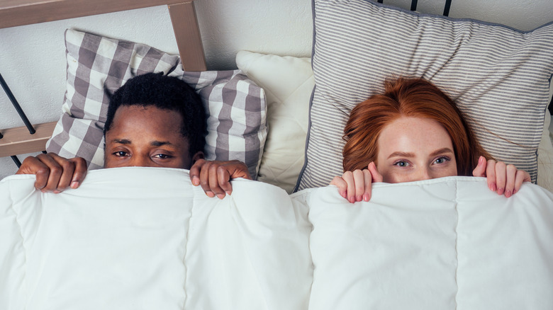 couple covering faces in bed