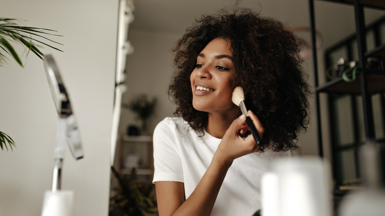 woman applying makeup with brush on cheeks