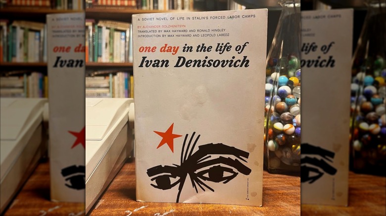 A book sits in front of a rustic bookcase and lamp filled with marbles in the background
