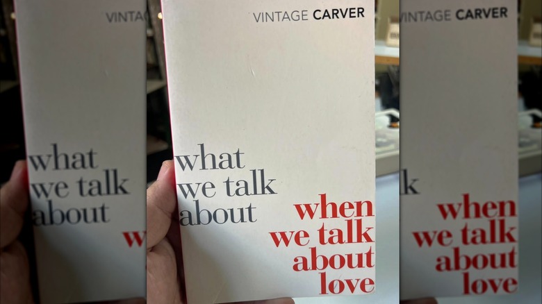 A hand holding up a white book with orange font titled 'What We Talk About When We Talk About Love'