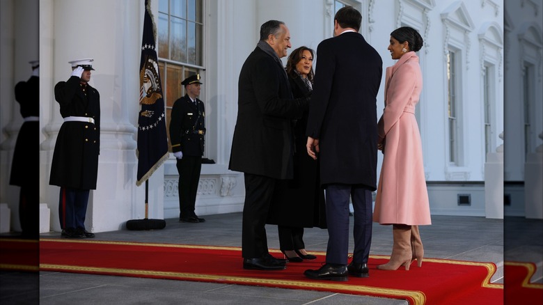Usha Vance stands at the presidential inauguration. She is wearing a long pink coat, tan gloves, and wide tan boots.