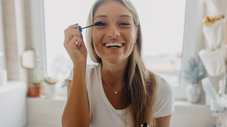 Woman applying mascara and smiling