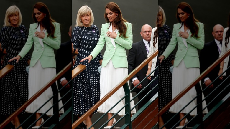 Kate Middleton walking down stairs wearing a white pleated skirt and light-green jacket with white trim at Wimbledon in 2023.