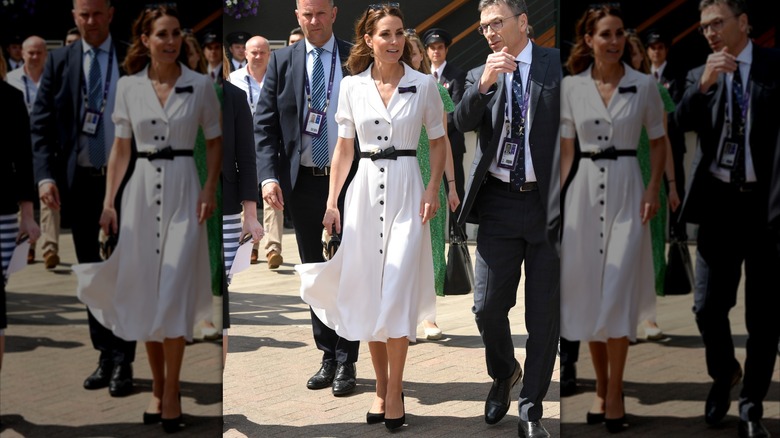 Kate Middleton wearing a white dress with black buttons and a black belt at Wimbledon in 2019.