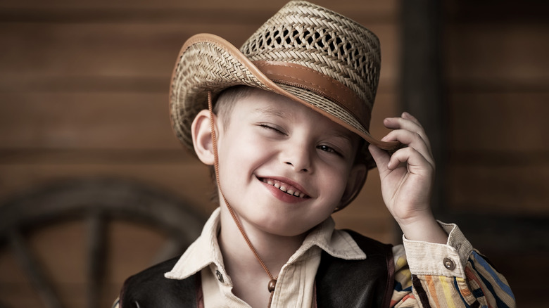 A kid winks and smiles dressed in Western attire