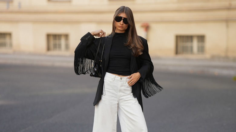 A woman wearing a black fringe blazer and white jeans.