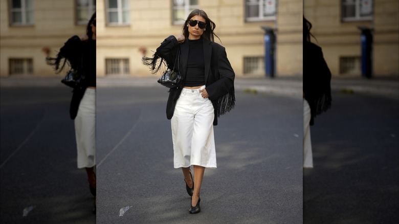 A woman wearing a black fringe blazer and white wide-leg culottes.