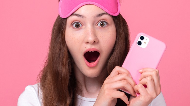 Girl with eye mask is shocked while holding pink phone