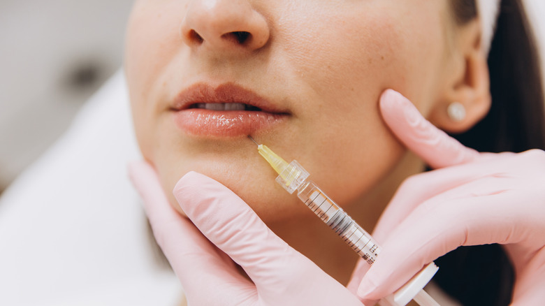 A beautician injecting filler into a woman's lips