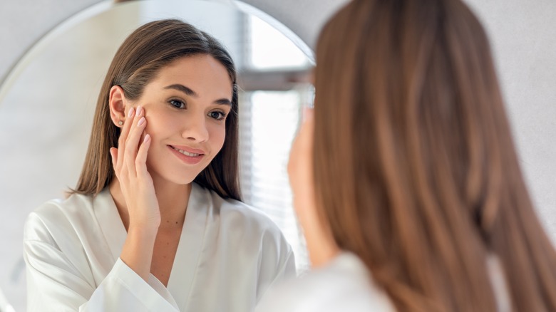 smiling young woman touching face looking in mirror