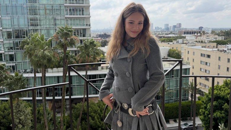 Skywalker Hughes posing in a gray peacoat on a balcony